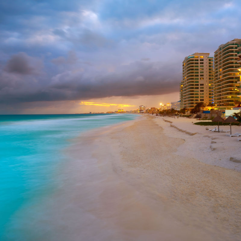 Puesta de sol en una playa de Cancún con un resort en el fondo