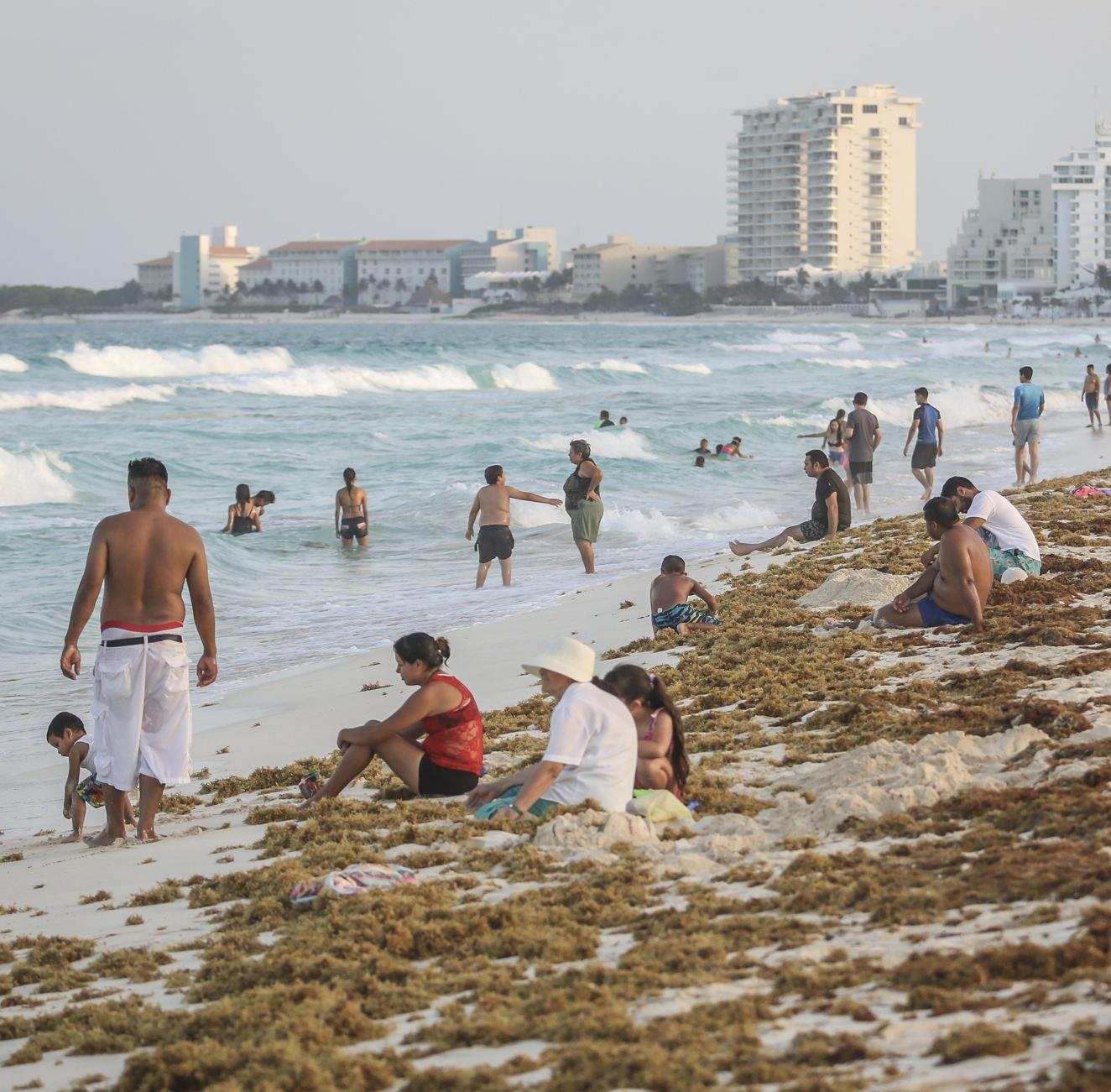 Los turistas se sientan en Sargassum en Cancún Beach