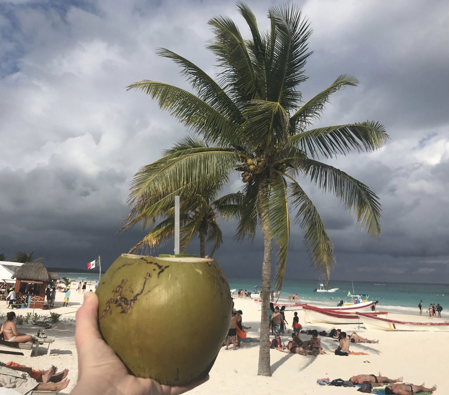 Mano sosteniendo un coco abierto en las nubes de tormenta de la playa del Caribe

