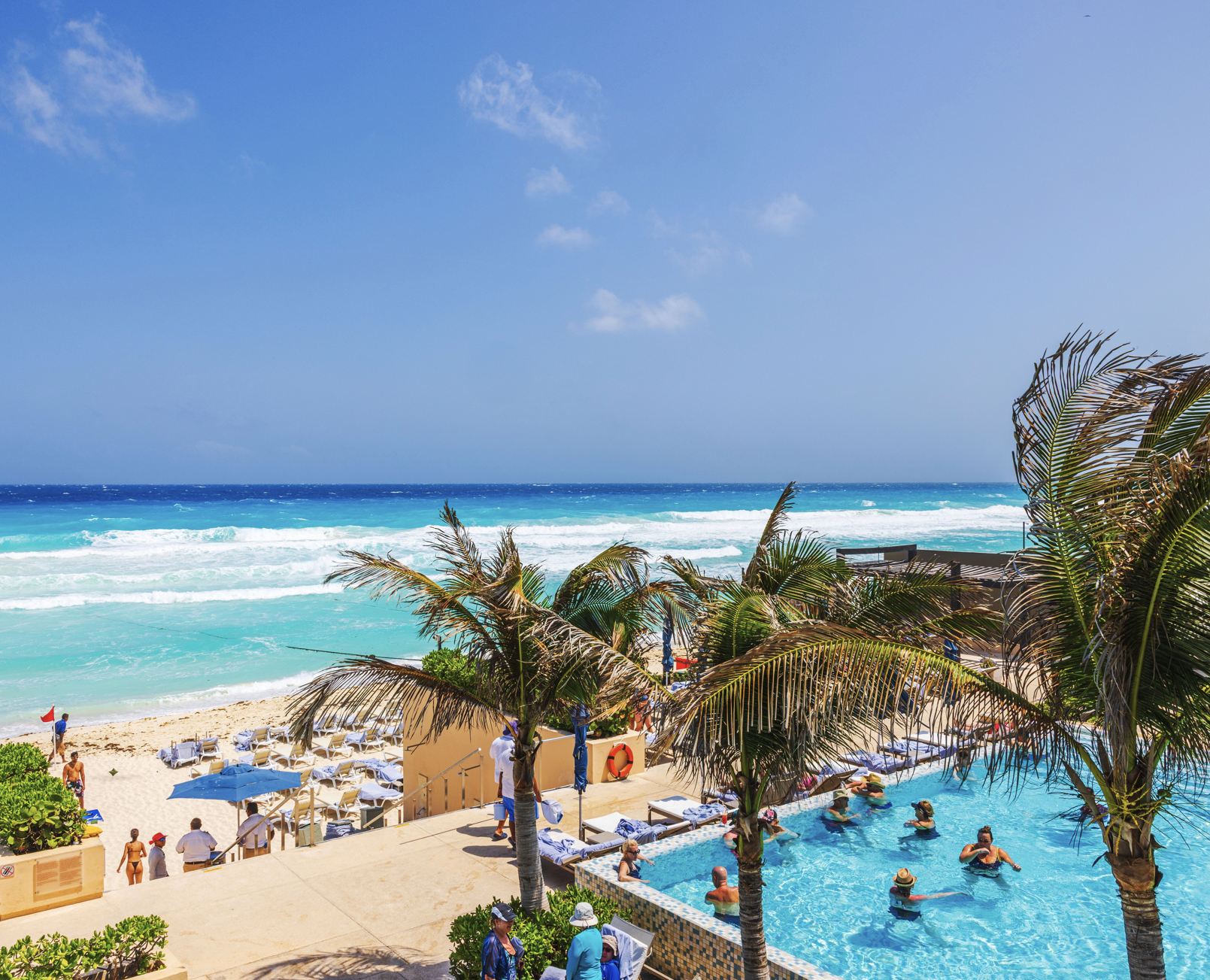 Las palmeras que se balancearon cerca de la piscina del resort con vistas a las olas turquesas del mar Caribe con tumbonas y a los beachs. México. Cancún.