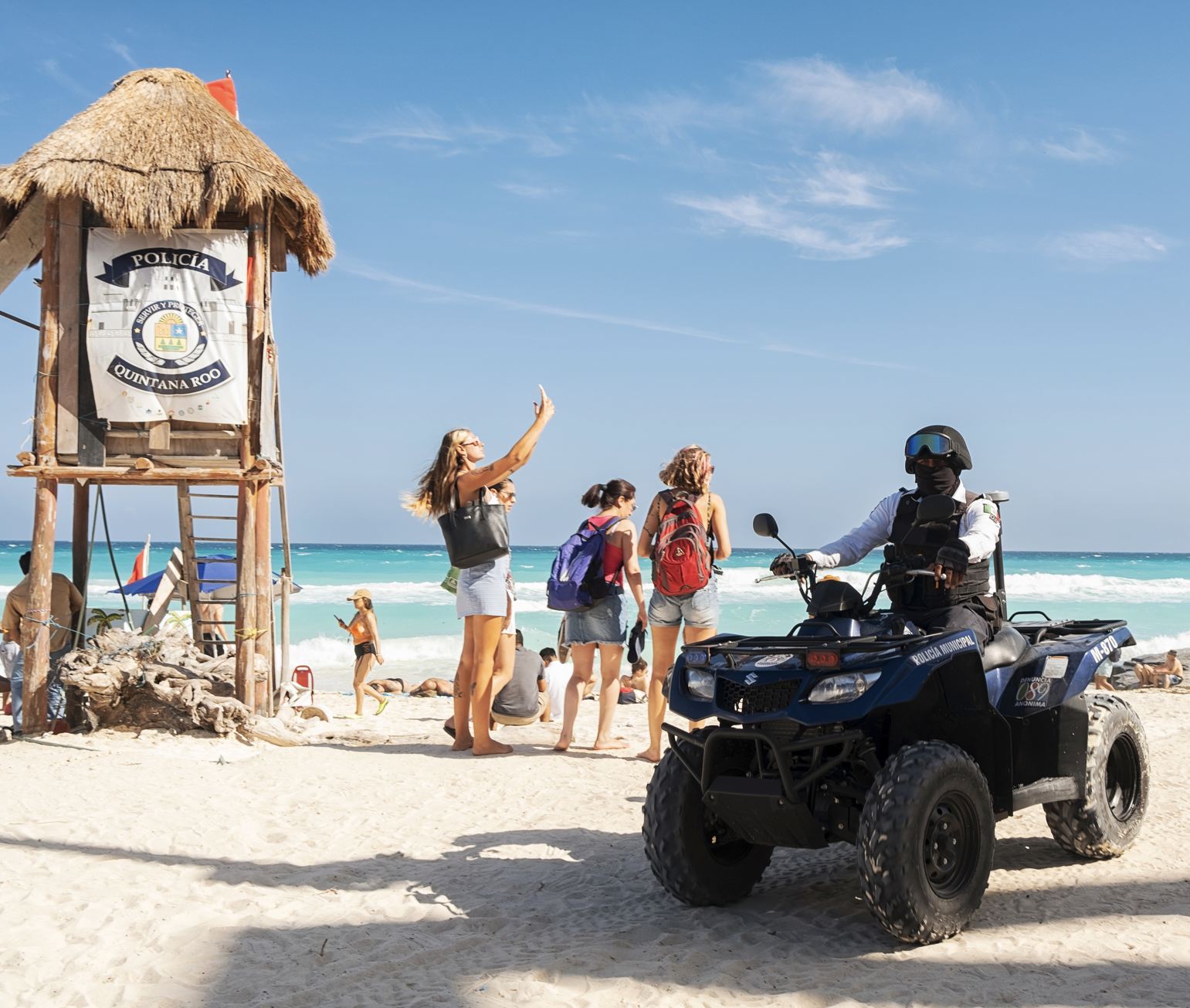 Oficial de policía en la playa de Cancún en ATV con turistas saludando