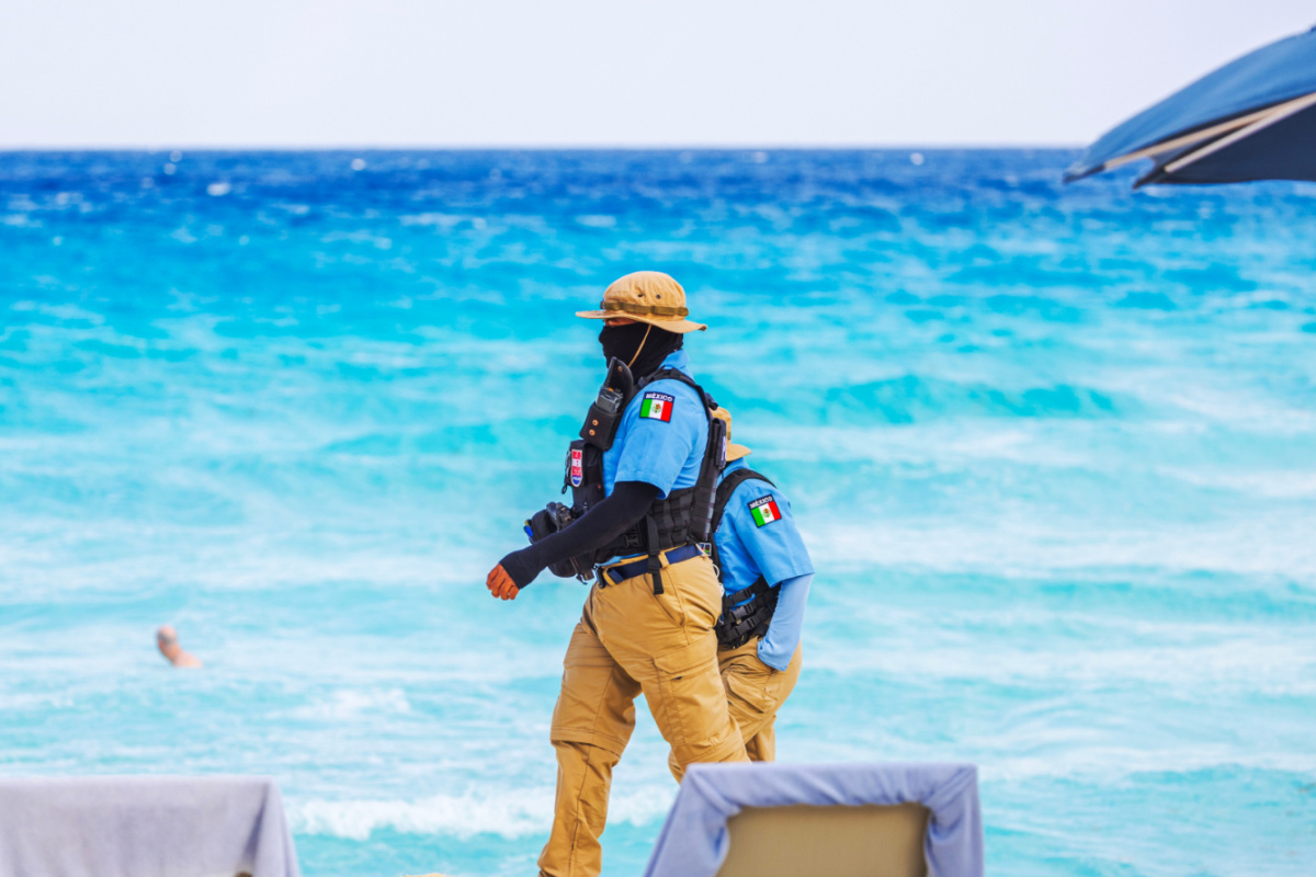 Oficiales de policía con equipo táctico patrullando una playa de arena cerca del mar turquesa del Caribe. Cancún. México.