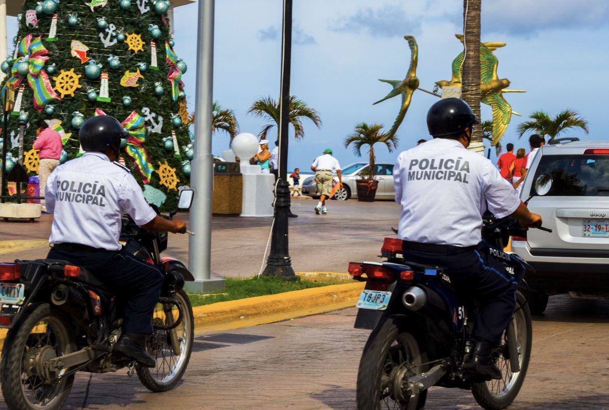 Destacados 2 POLICÍAS MUNICIPAL EN MOTO EN COZUMEL CON ÁRBOL DE NAVIDAD DECORADO y turistas caminando en un día soleado