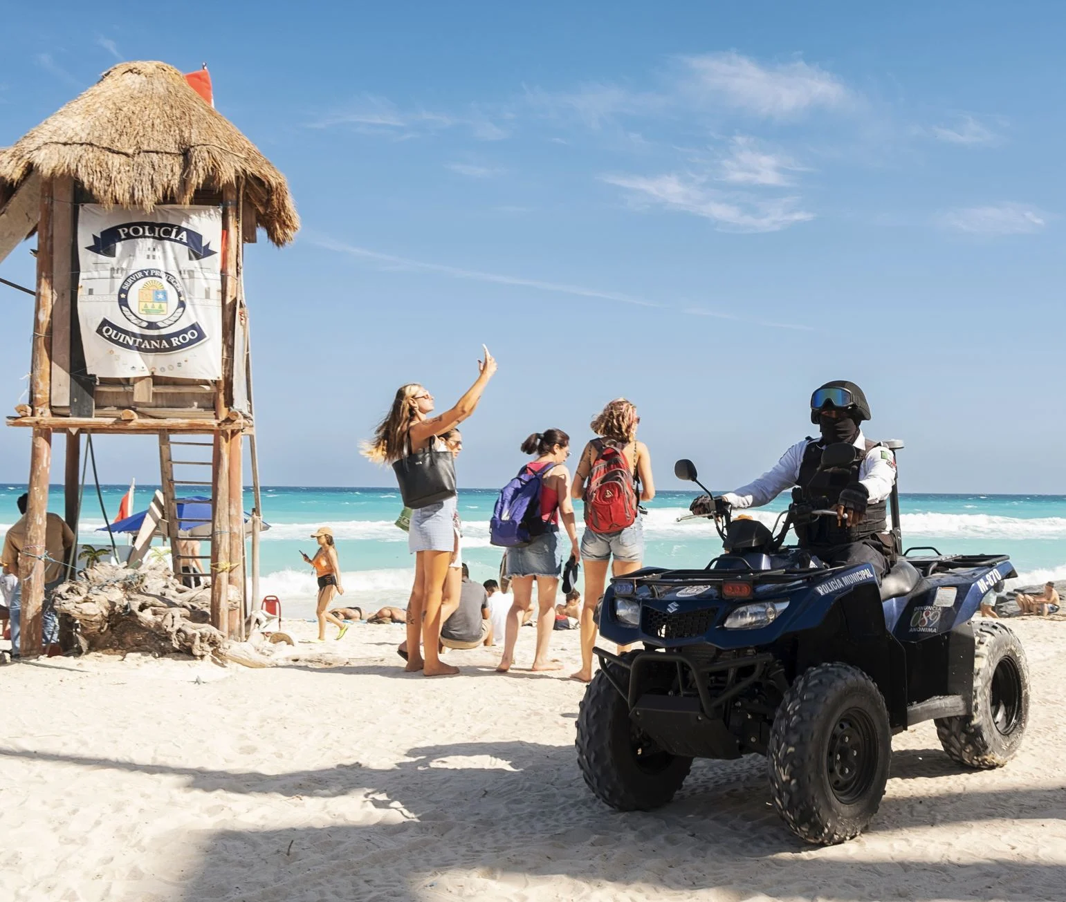 Oficial de policía en la playa de Cancún en ATV con turistas saludando