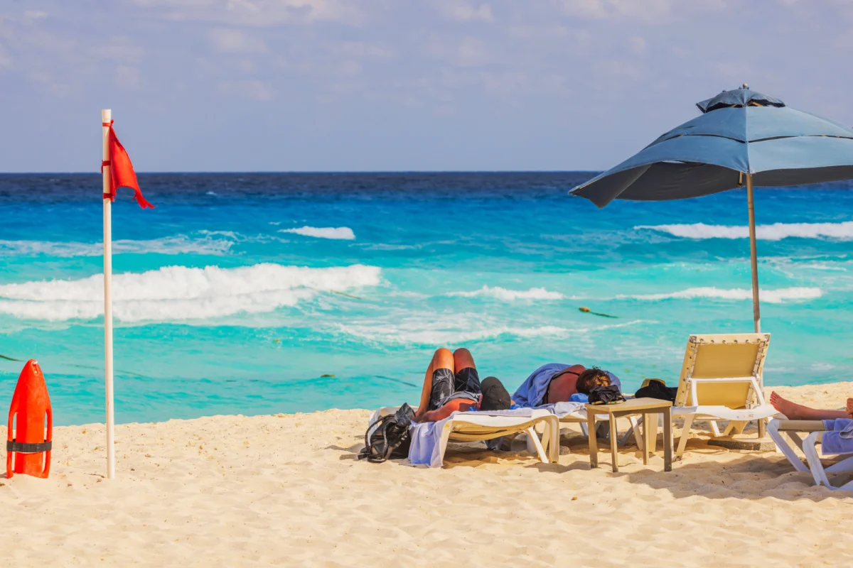 Playa de Cancún con una bandera roja ondeando al viento y turistas descansando