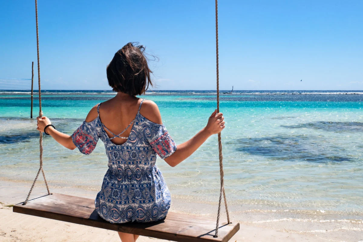 Joven morena tumbada en un columpio en una playa paradisíaca de la costa mexicana, rodeada de arena blanca y agua turquesa, en el pueblo de Mahahual, en Quintana Roo, México.
